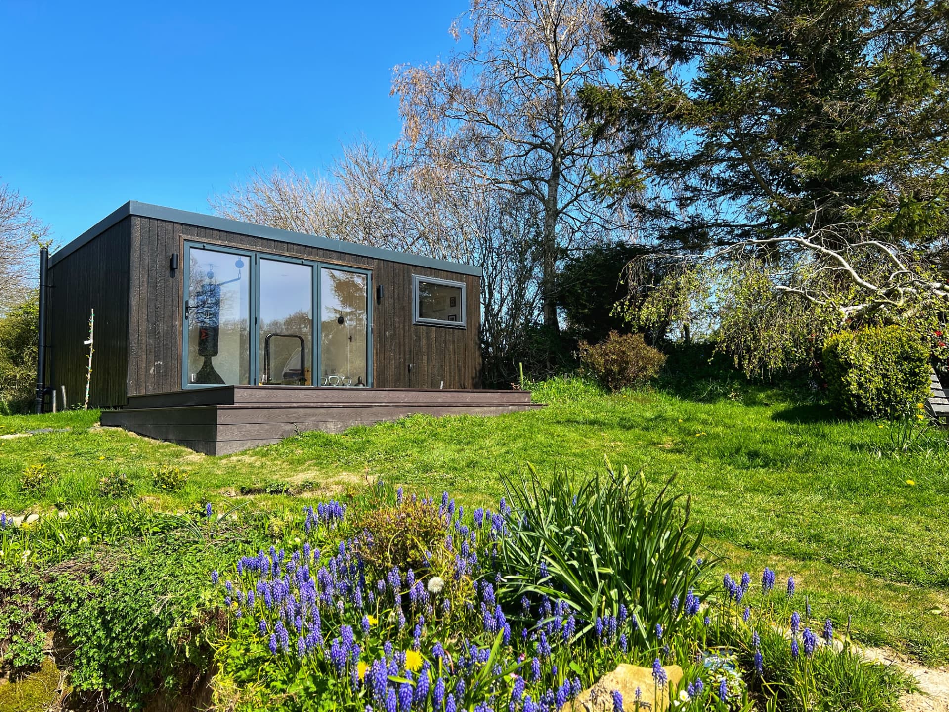 Charred timber clad garden room with sliding doors on a raised deck in a spring garden