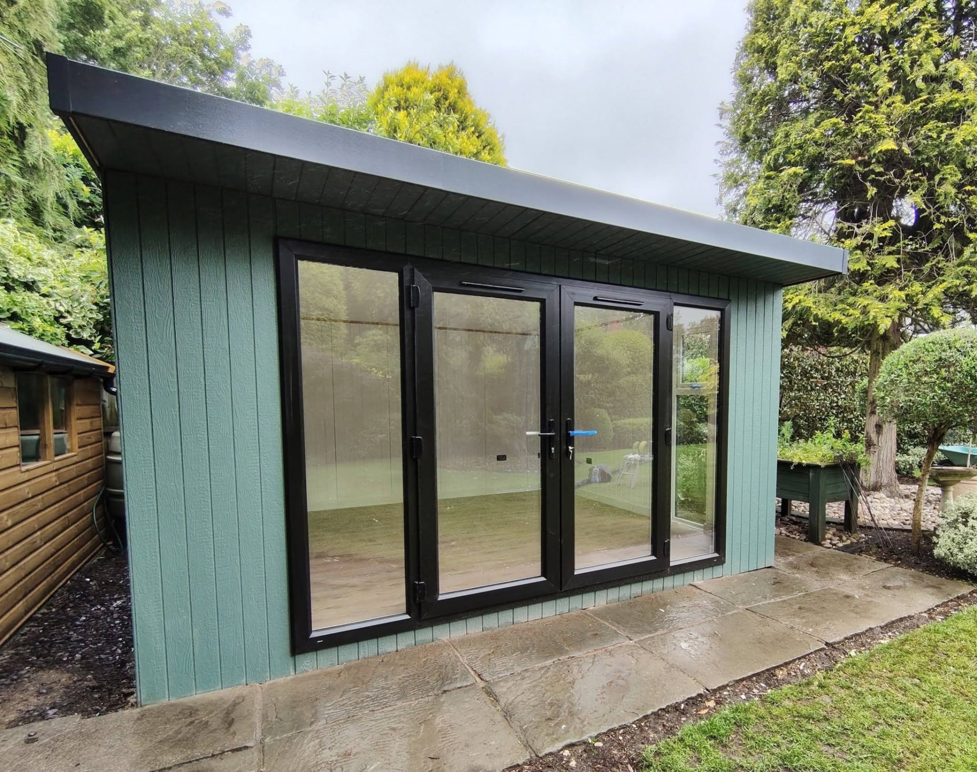 Custom green ToughWood garden room with black bifold doors on a stone patio