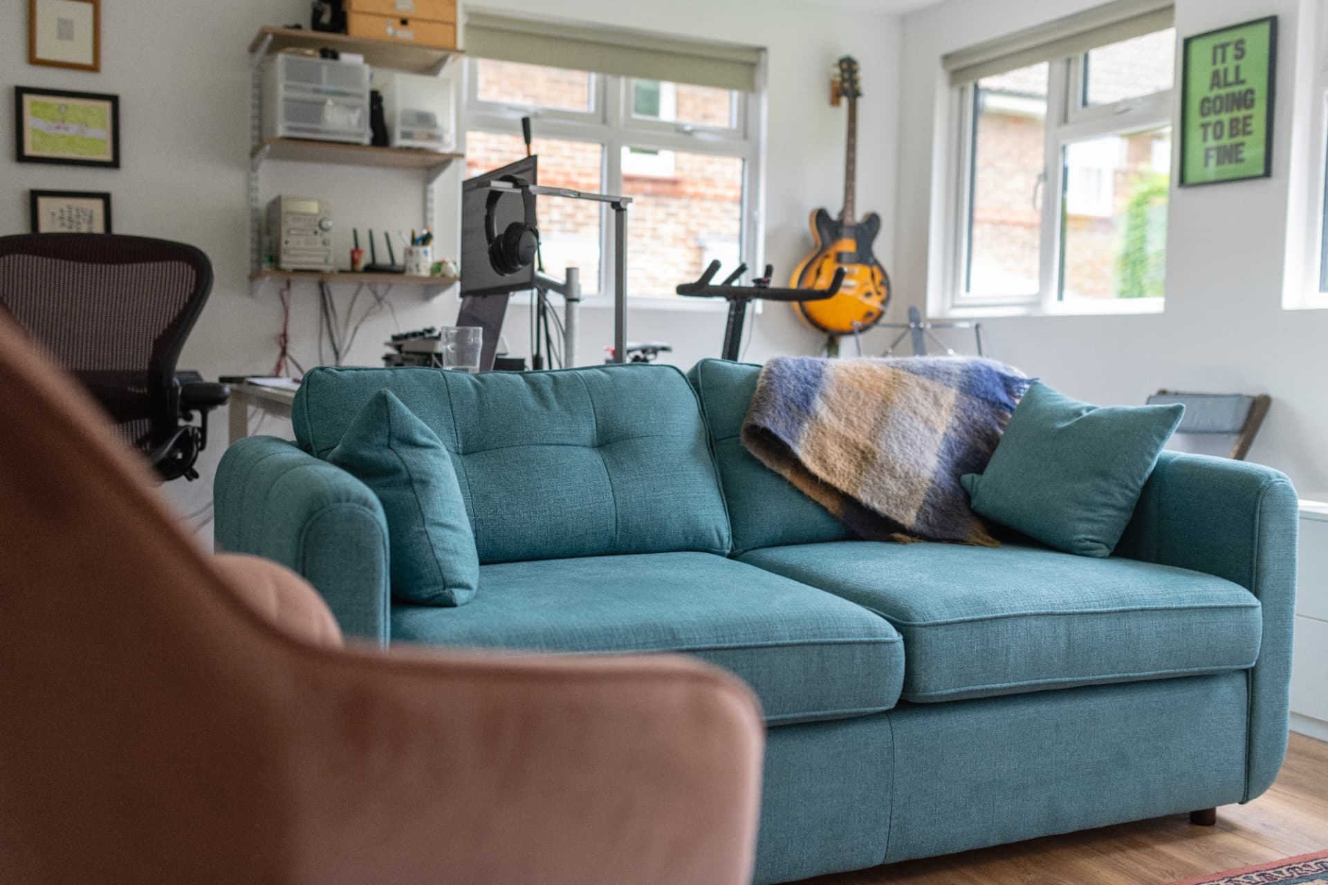 Garden room snug with a teal sofa, desk, exercise bike and guitar