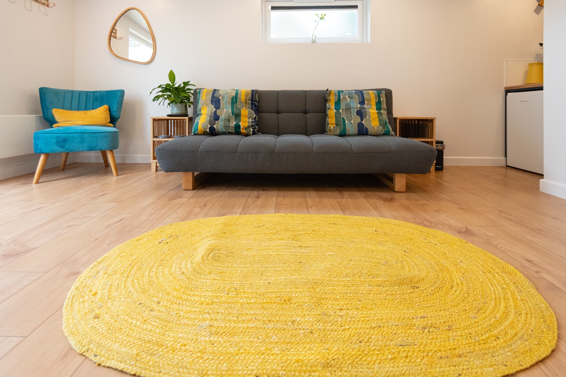 Garden room seating area with a teal armchair, grey sofa bed and yellow jute rug