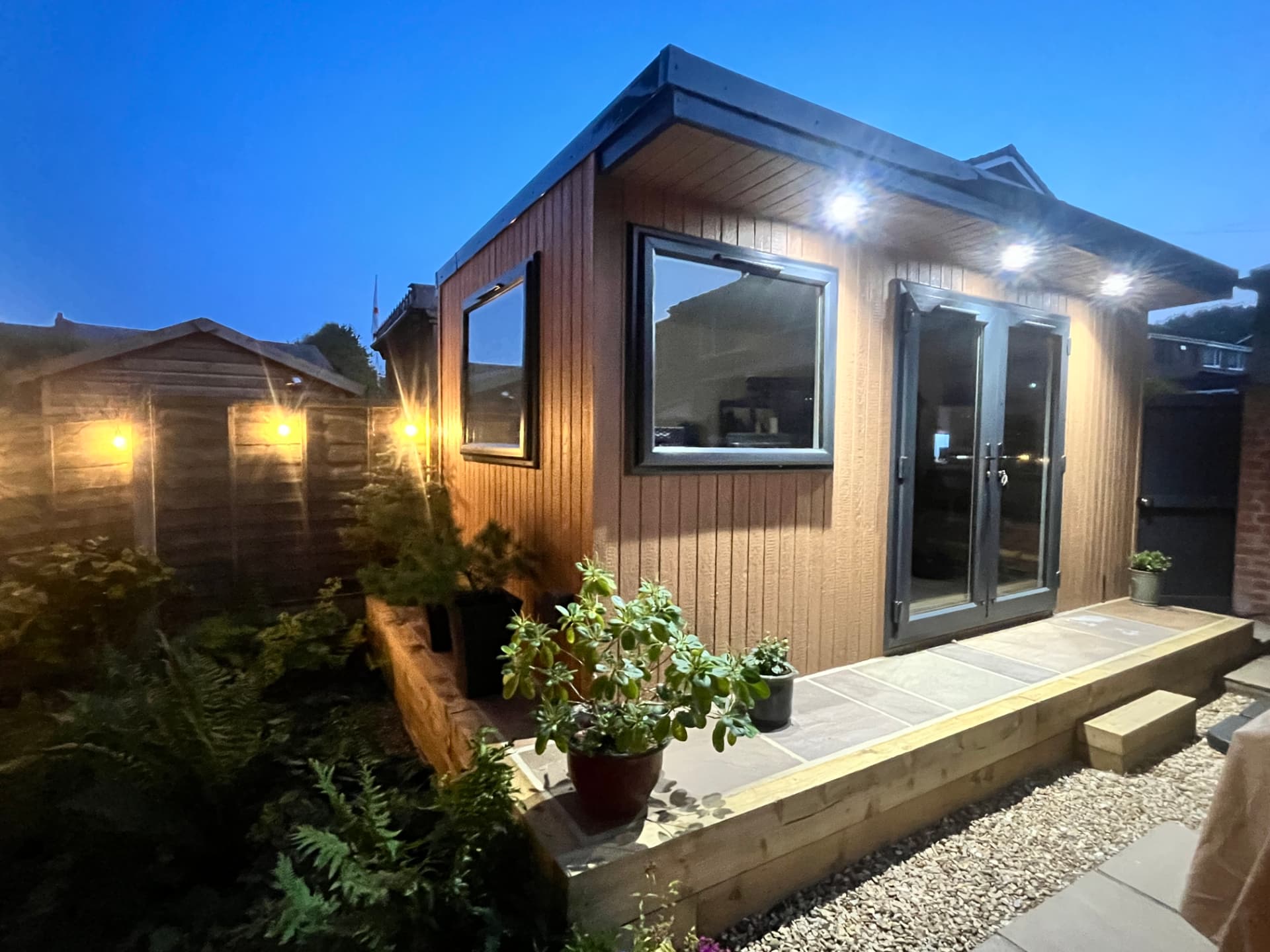 Cedar ToughWood garden room glowing at blue hour beside a planted border