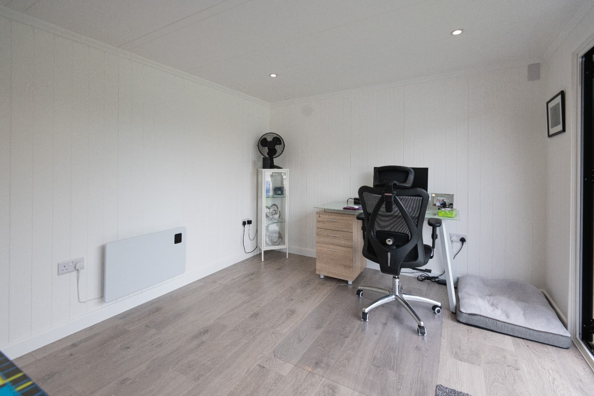 Bright white garden office with a glass desk, drawers and dog bed