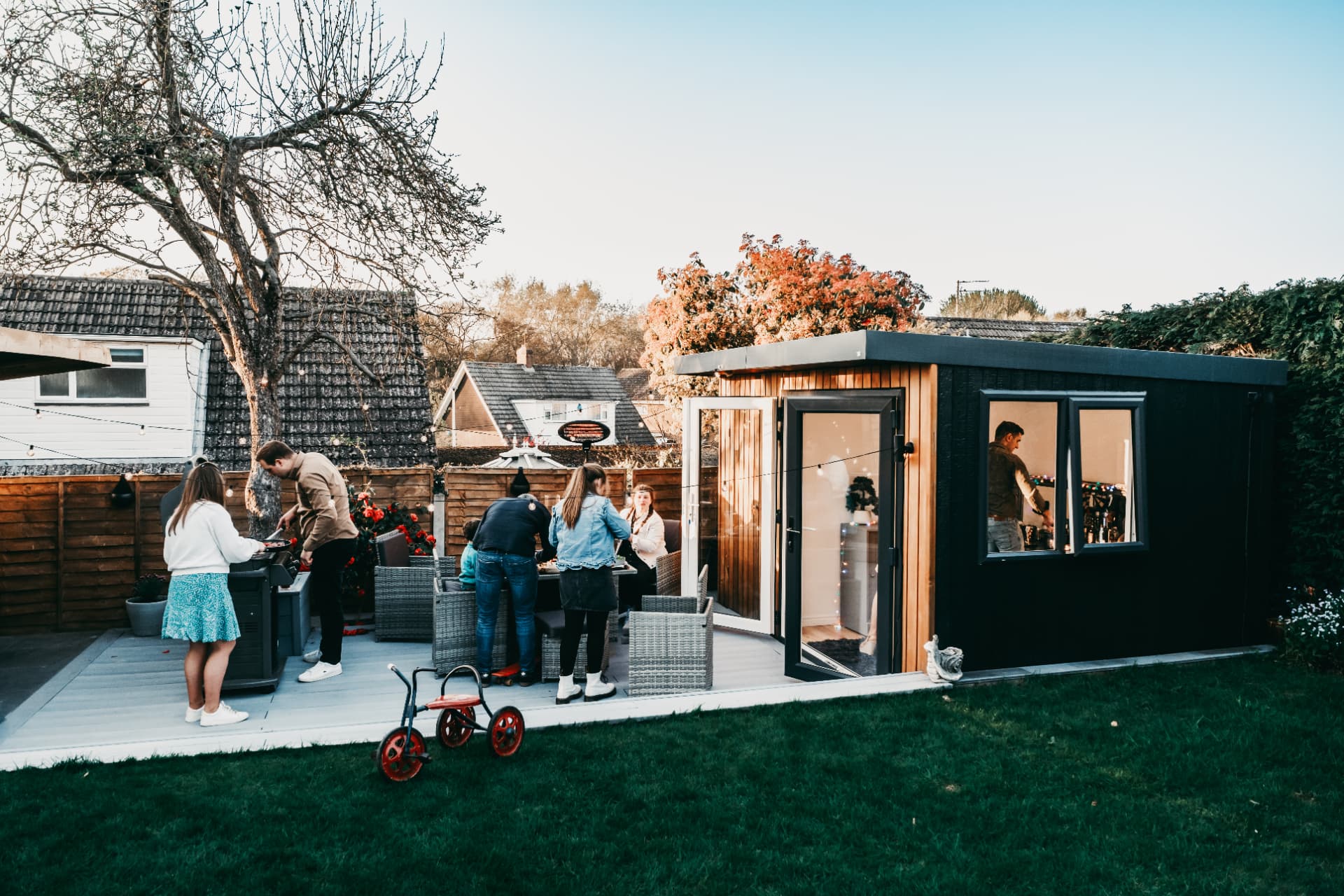 Family barbecue at golden hour outside a black and cedar clad garden room
