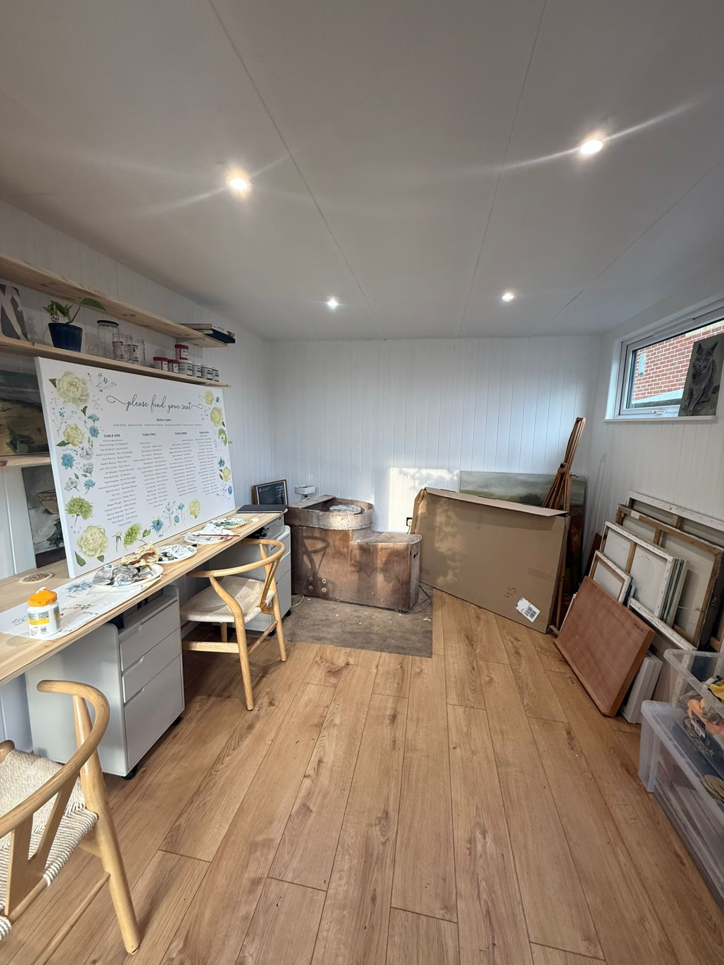 Garden room fitted out as an artist's studio with a long timber desk, canvases and open shelving