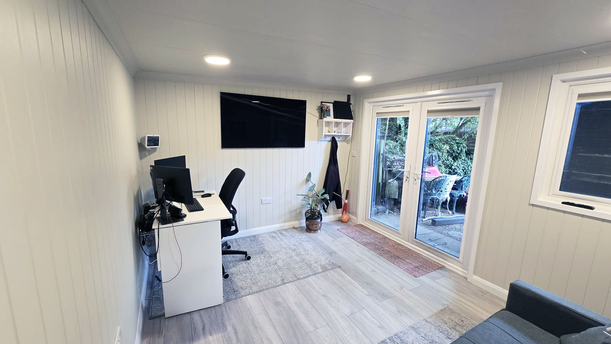 Garden room combining a desk workstation, wall TV and sofa with French doors to the patio