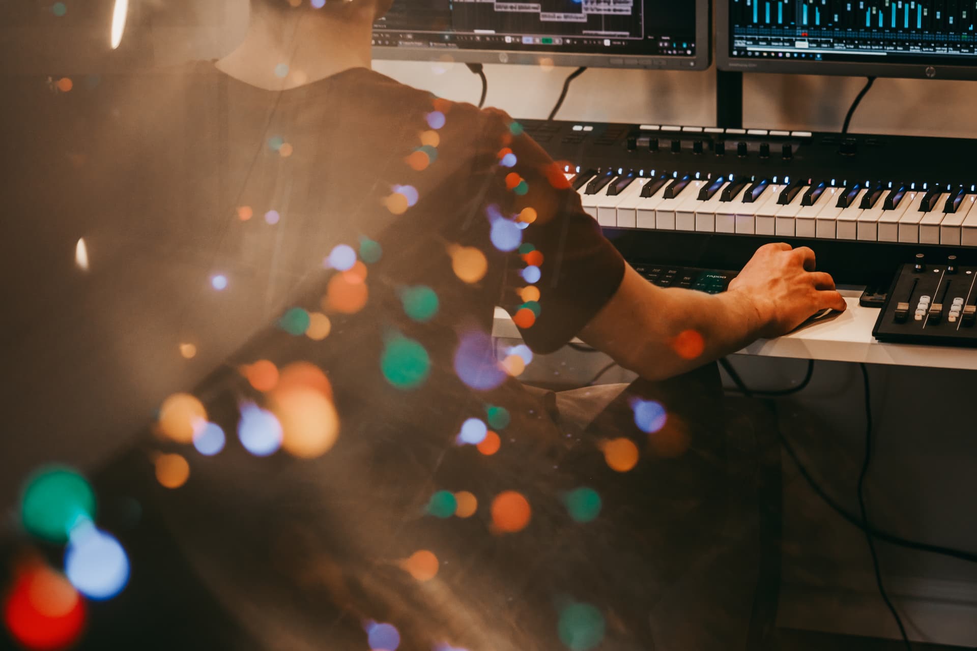 Hands at a MIDI keyboard and mixing desk in a garden recording studio