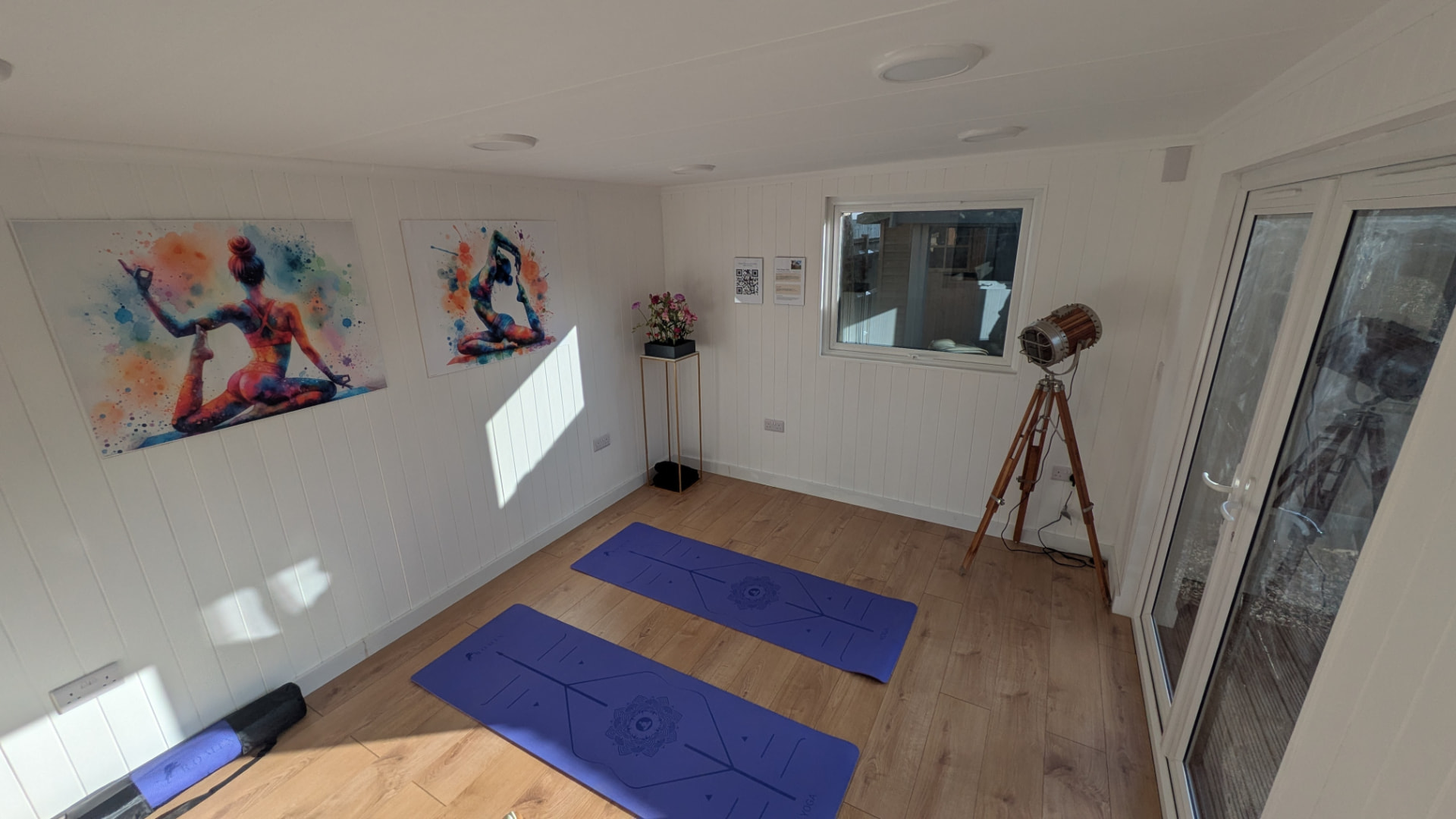 White panelled garden yoga studio with mats and framed yoga artwork