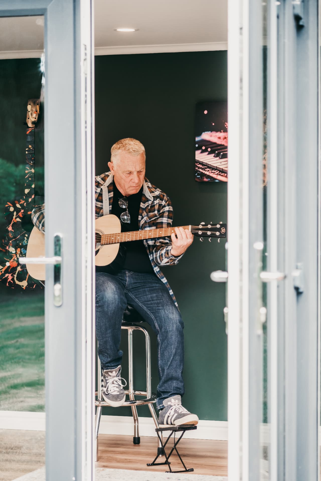 Guitarist playing inside a garden music room seen through open French doors