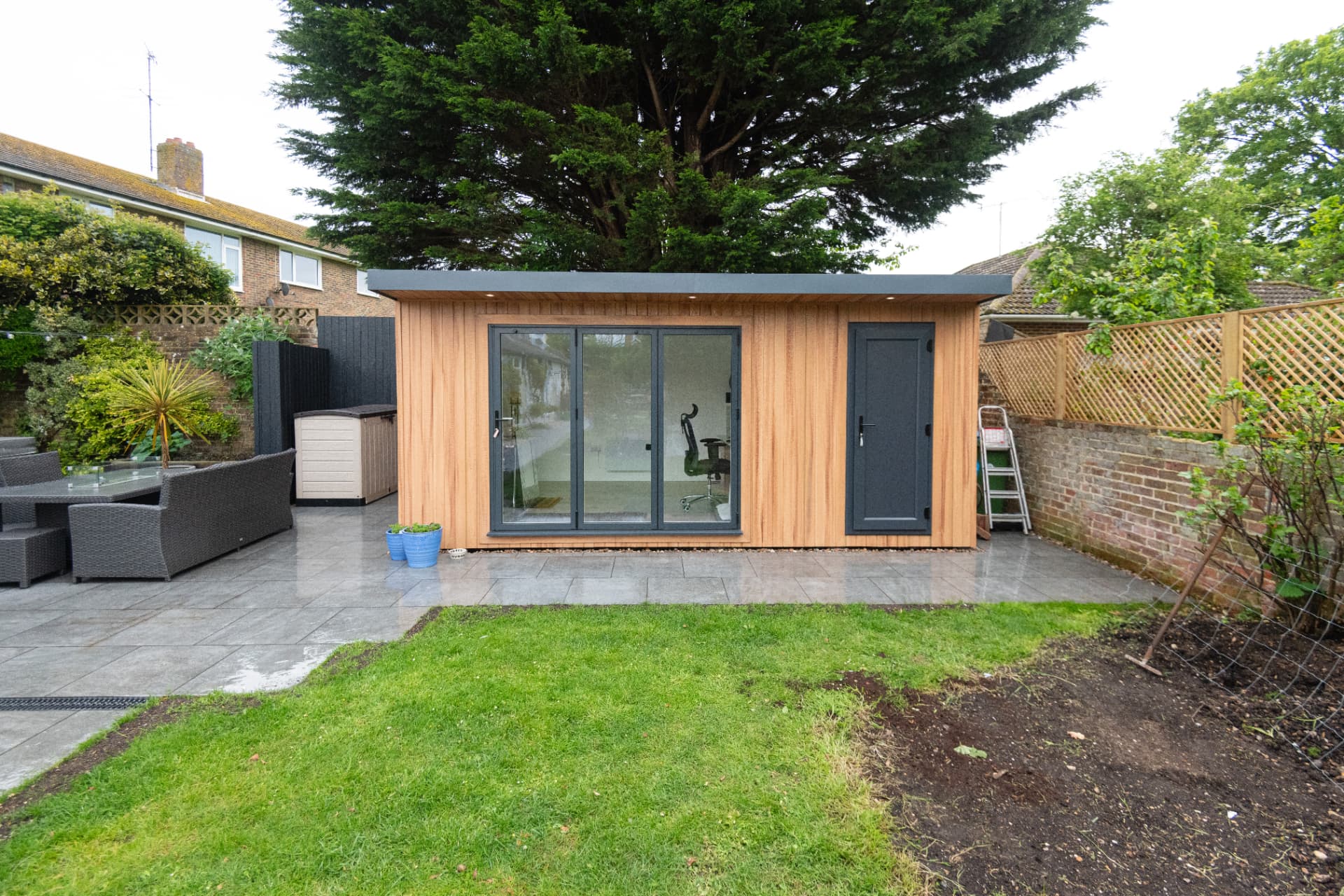 Cedar garden room across a lawn with patio furniture alongside