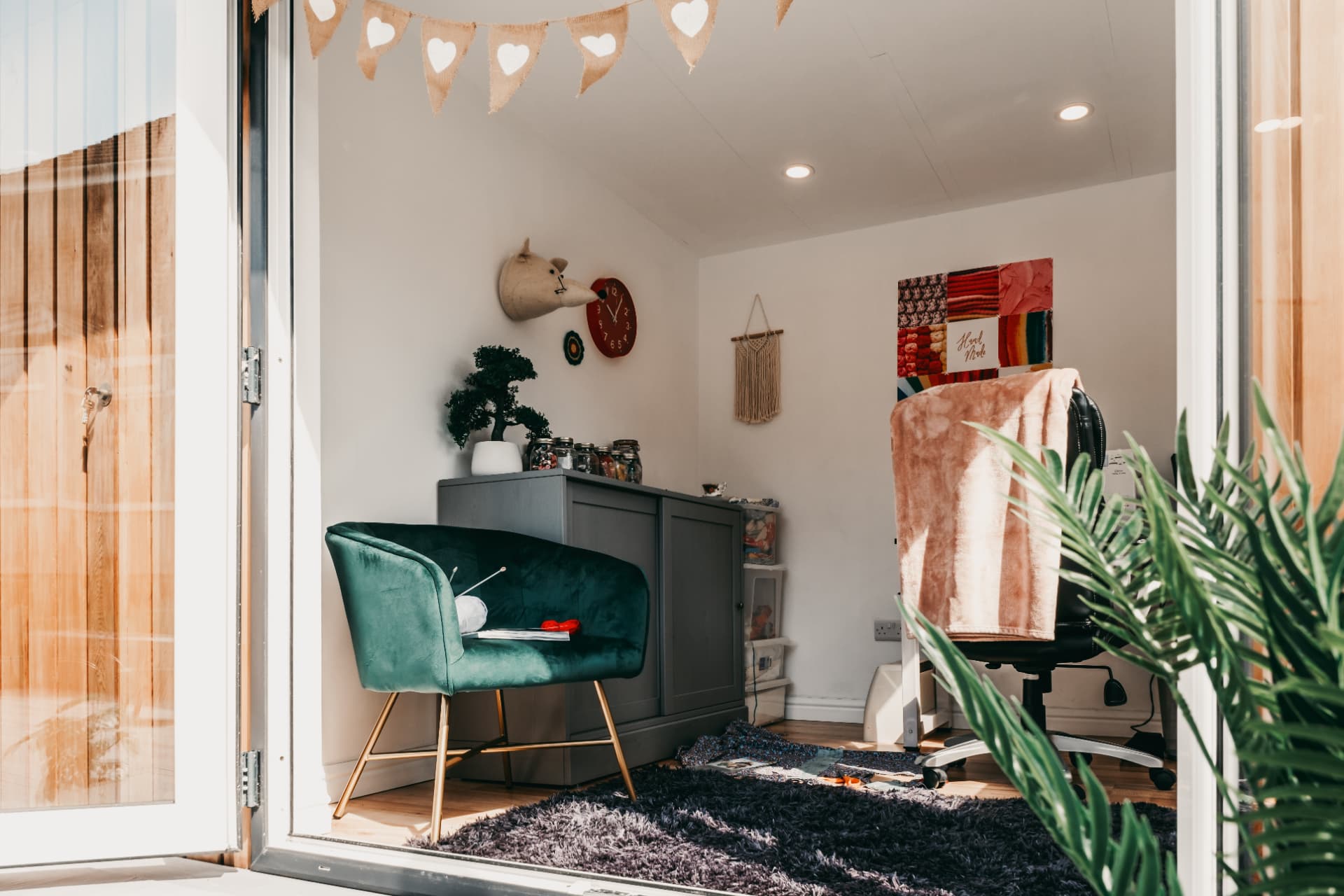 Garden room craft studio with a green velvet chair, storage and handmade wall art