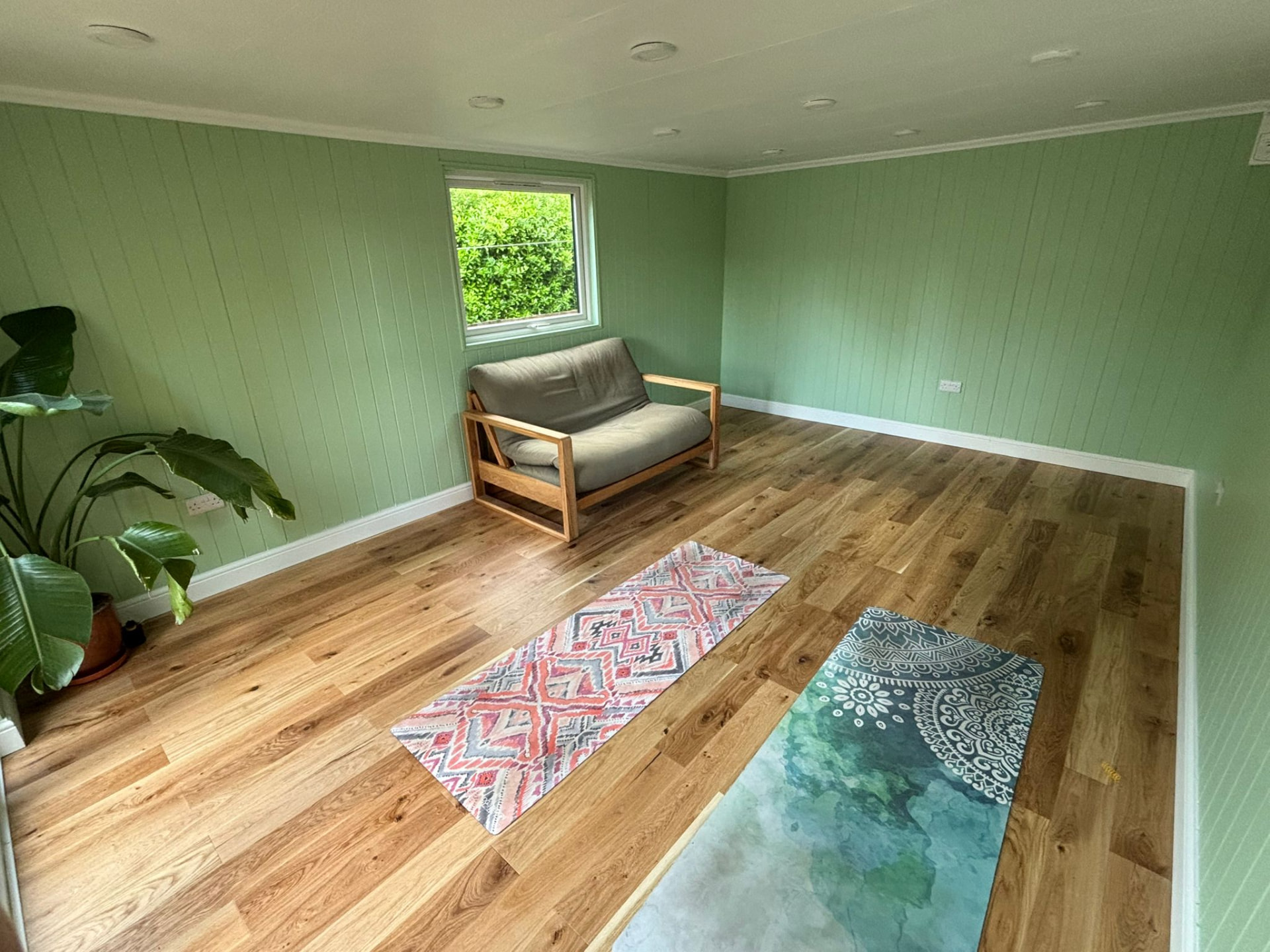 Sage green garden room interior used as a yoga and relaxation space with futon sofa