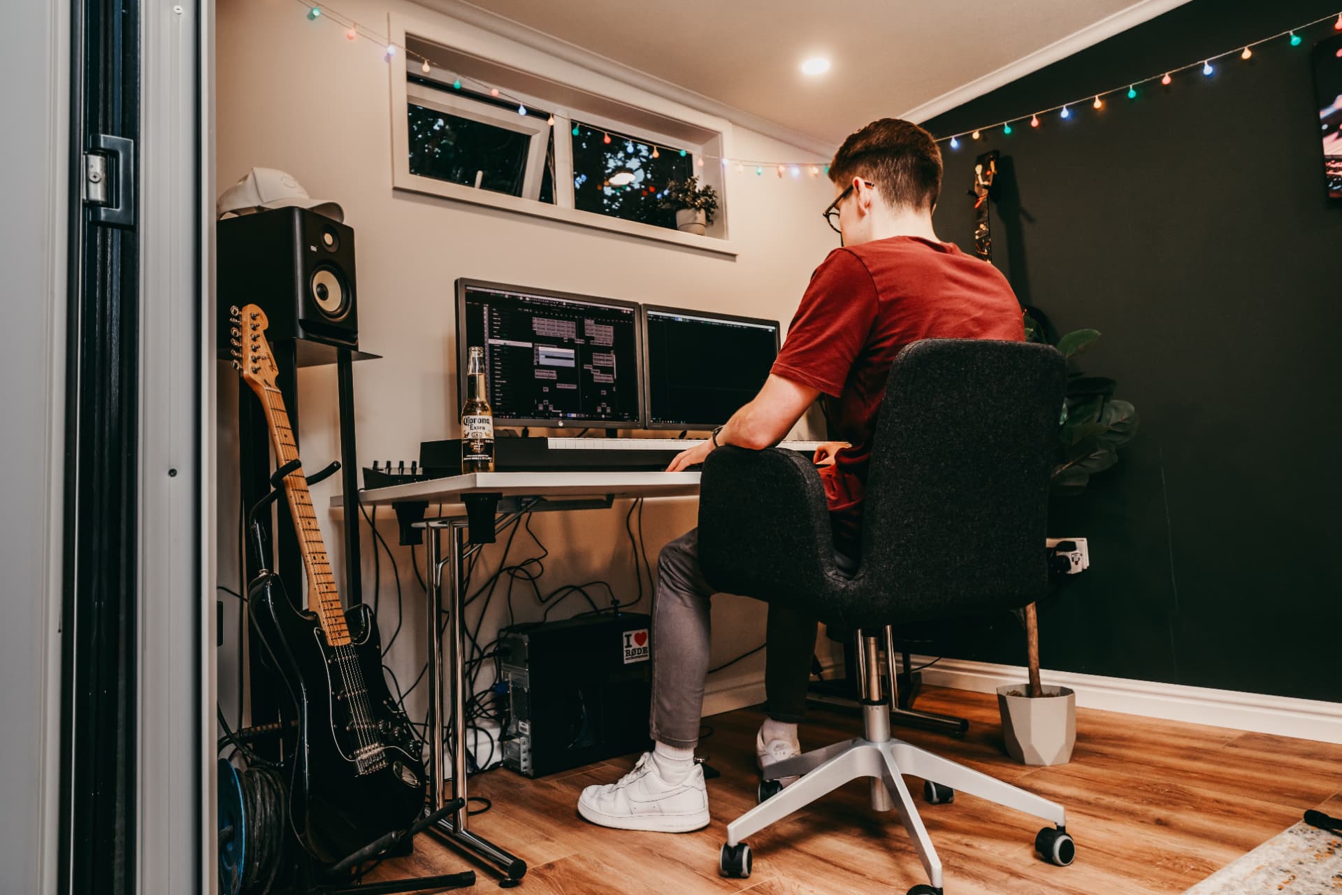 Producer at a garden studio desk with twin monitors, MIDI keyboard and guitars