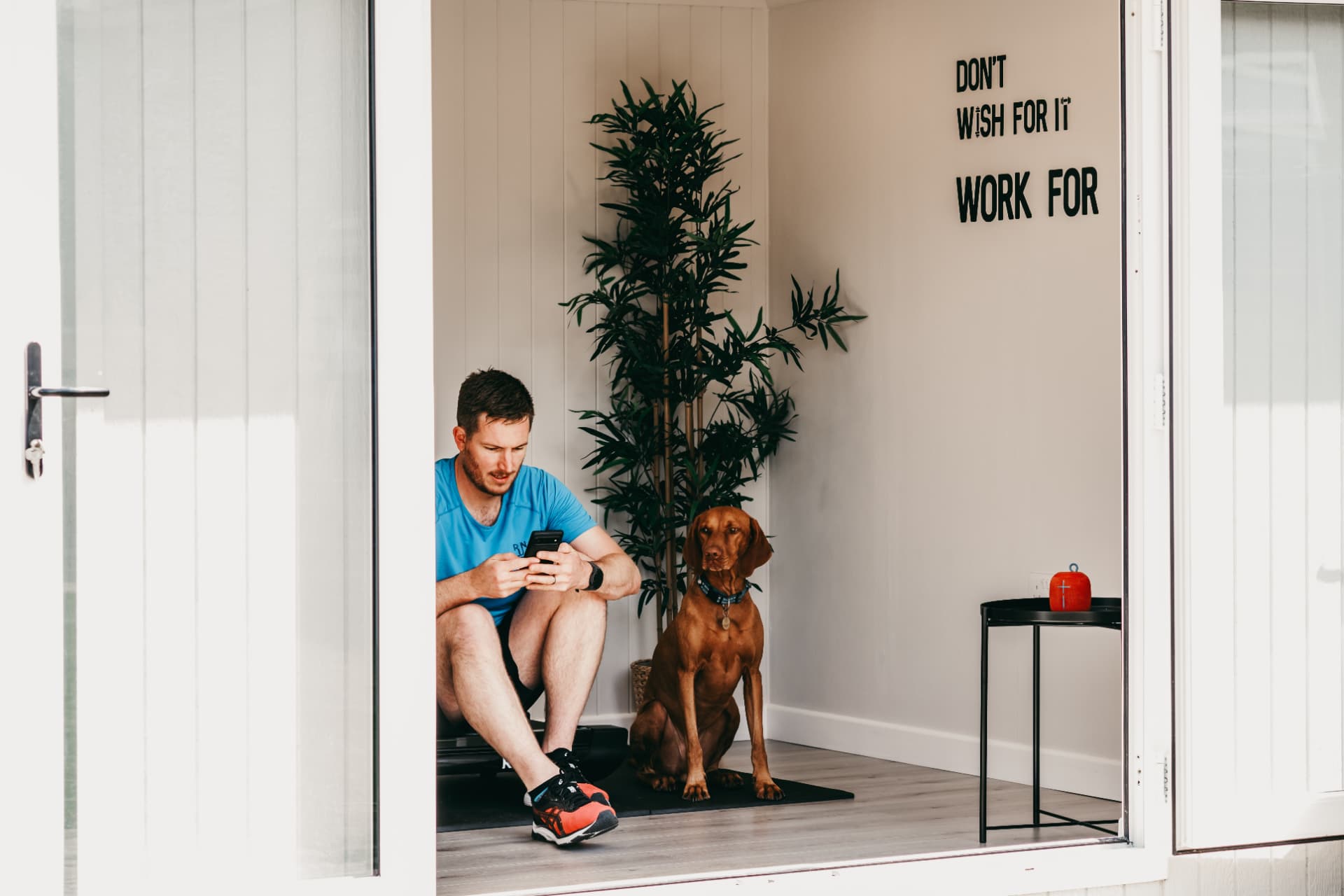 Man and his dog sitting in the doorway of a garden gym after a workout