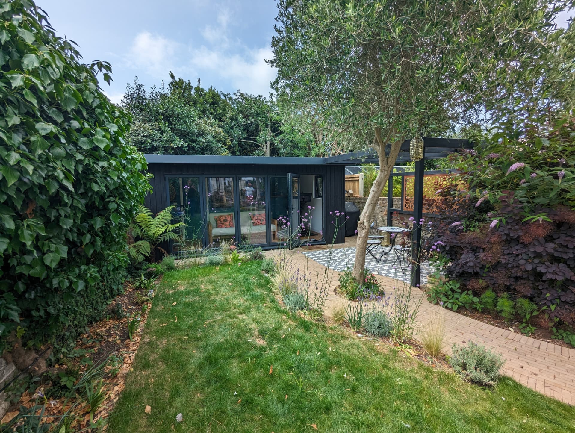 Granite ToughWood garden room set into a planted garden with a pergola and patio
