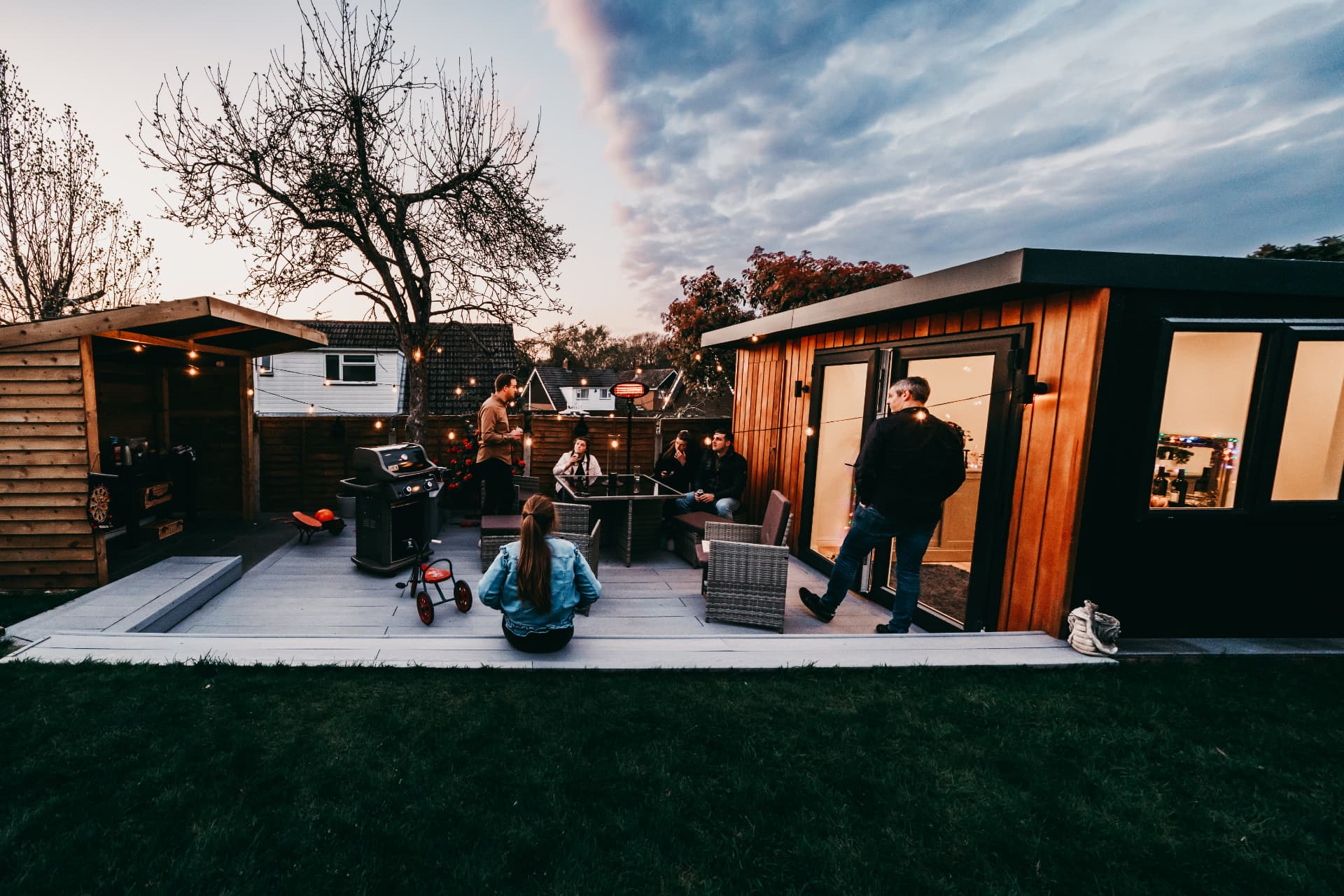 Friends and family relaxing on the deck at dusk outside a cedar clad garden room