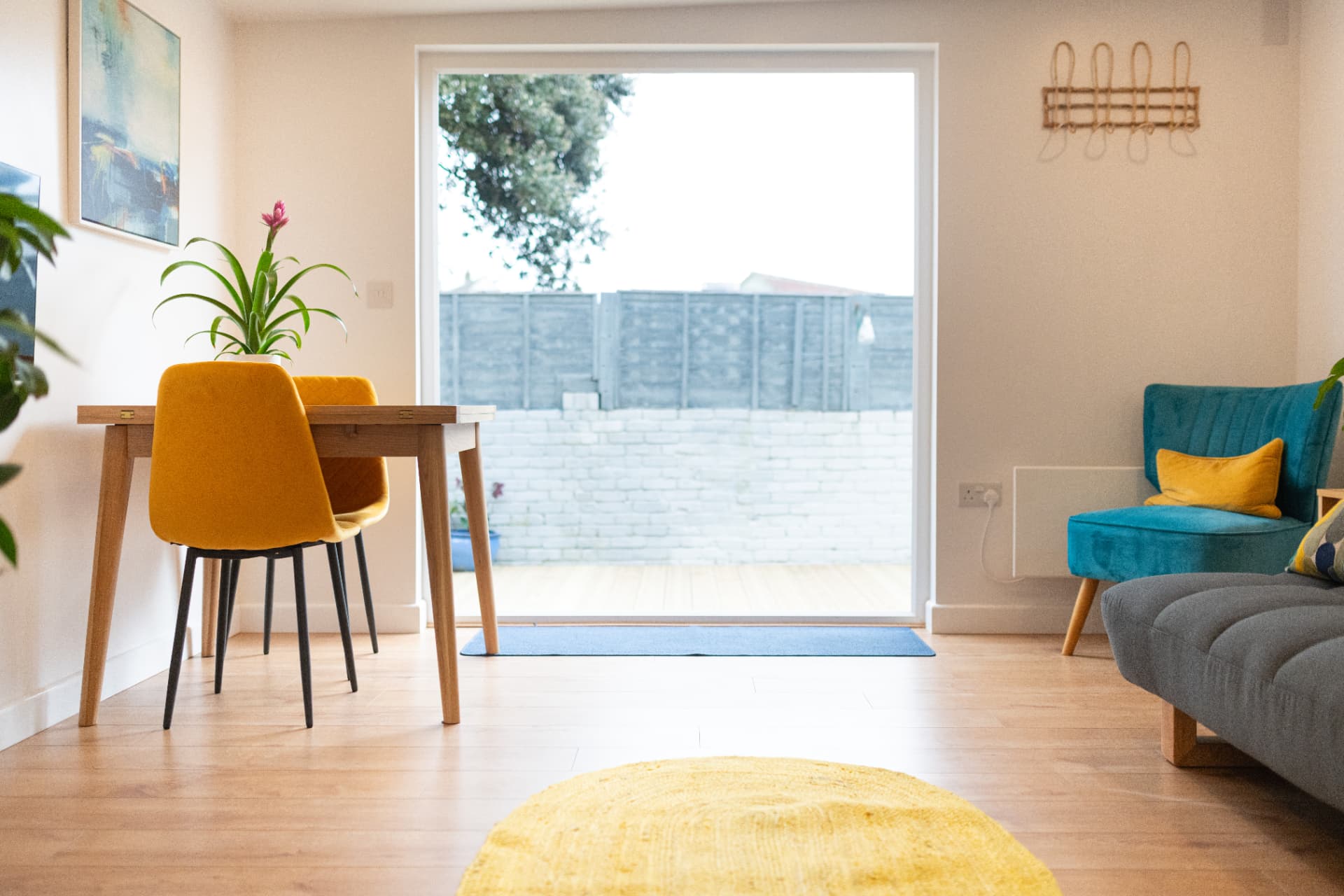 Dining table and chairs beside a full-height window looking onto the garden deck