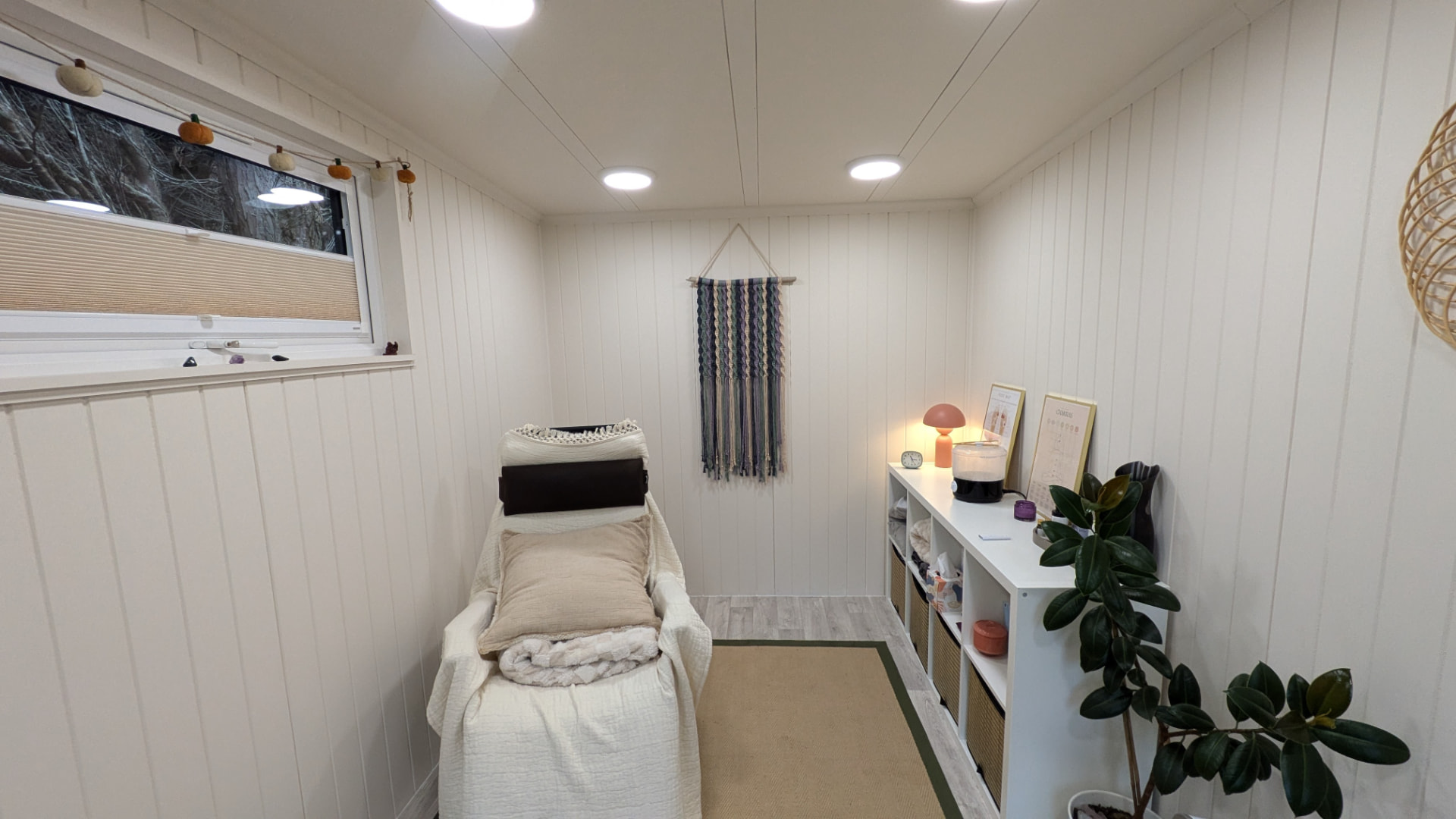 Garden room fitted out as a therapy treatment room with a couch, macrame wall hanging and storage