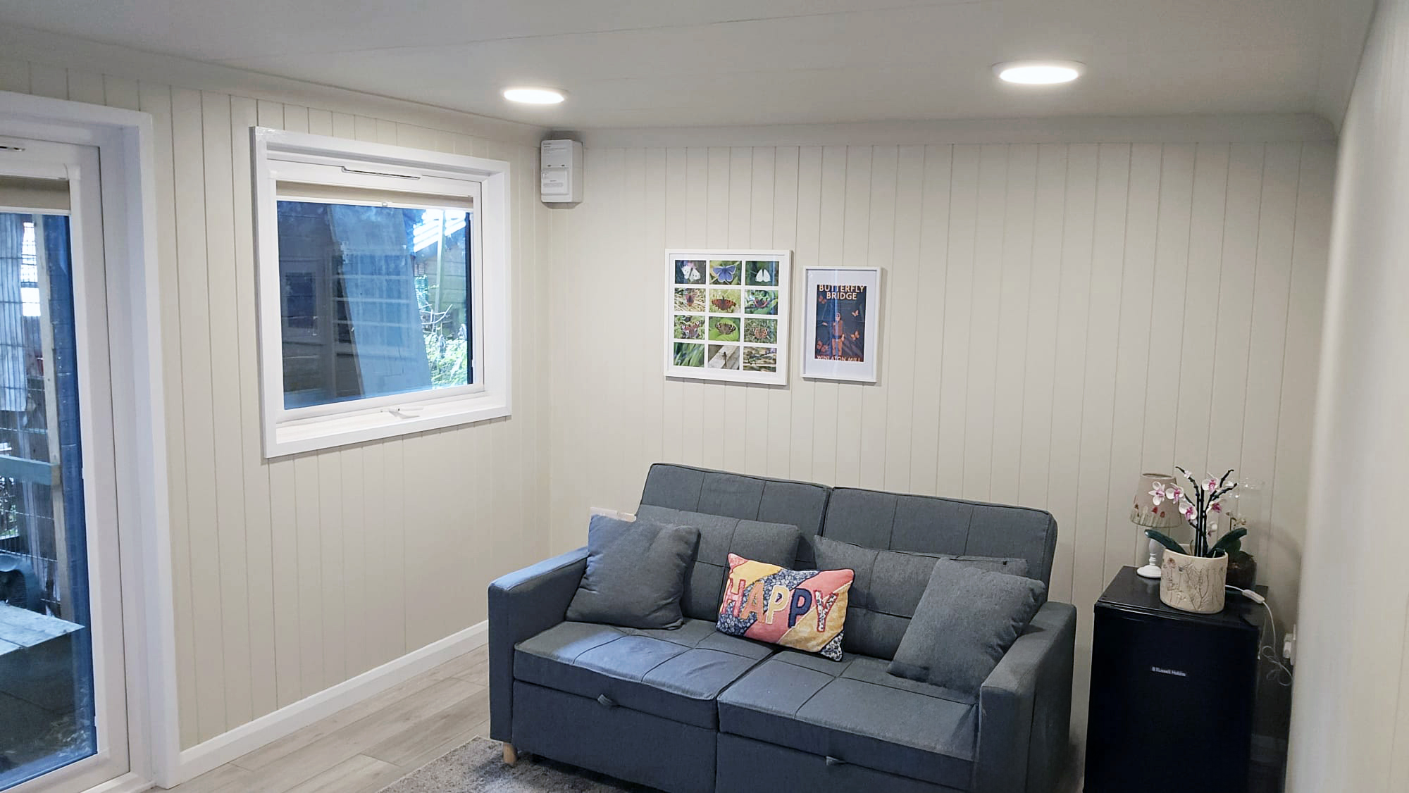 Cream panelled garden room lounge with a grey sofa bed and framed prints