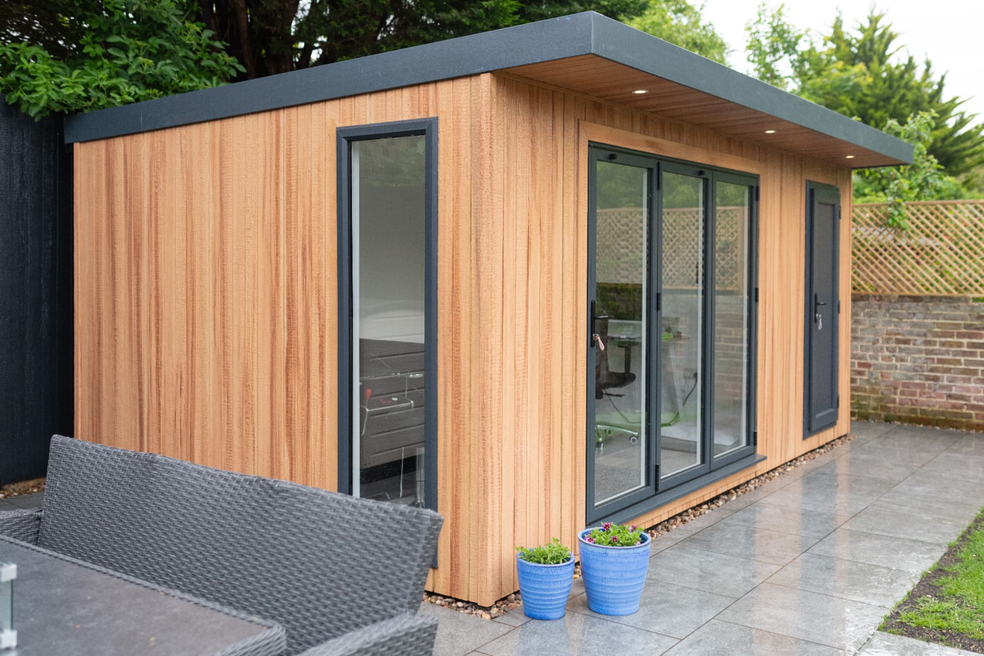 Cedar clad garden room home office with anthracite bifold doors open onto a patio