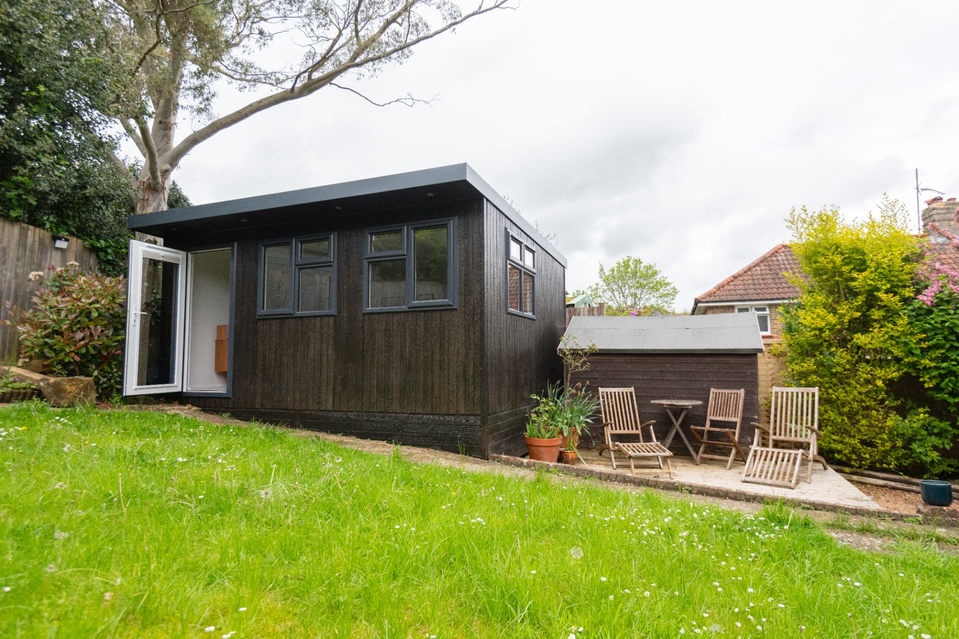 Burnt Oak clad garden room with white French doors open onto a lawn