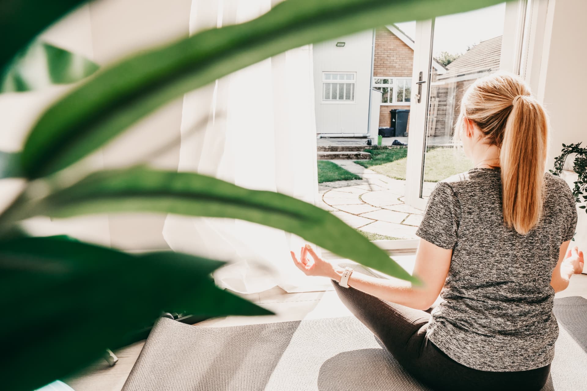 Woman meditating on a mat looking out through open doors onto the garden