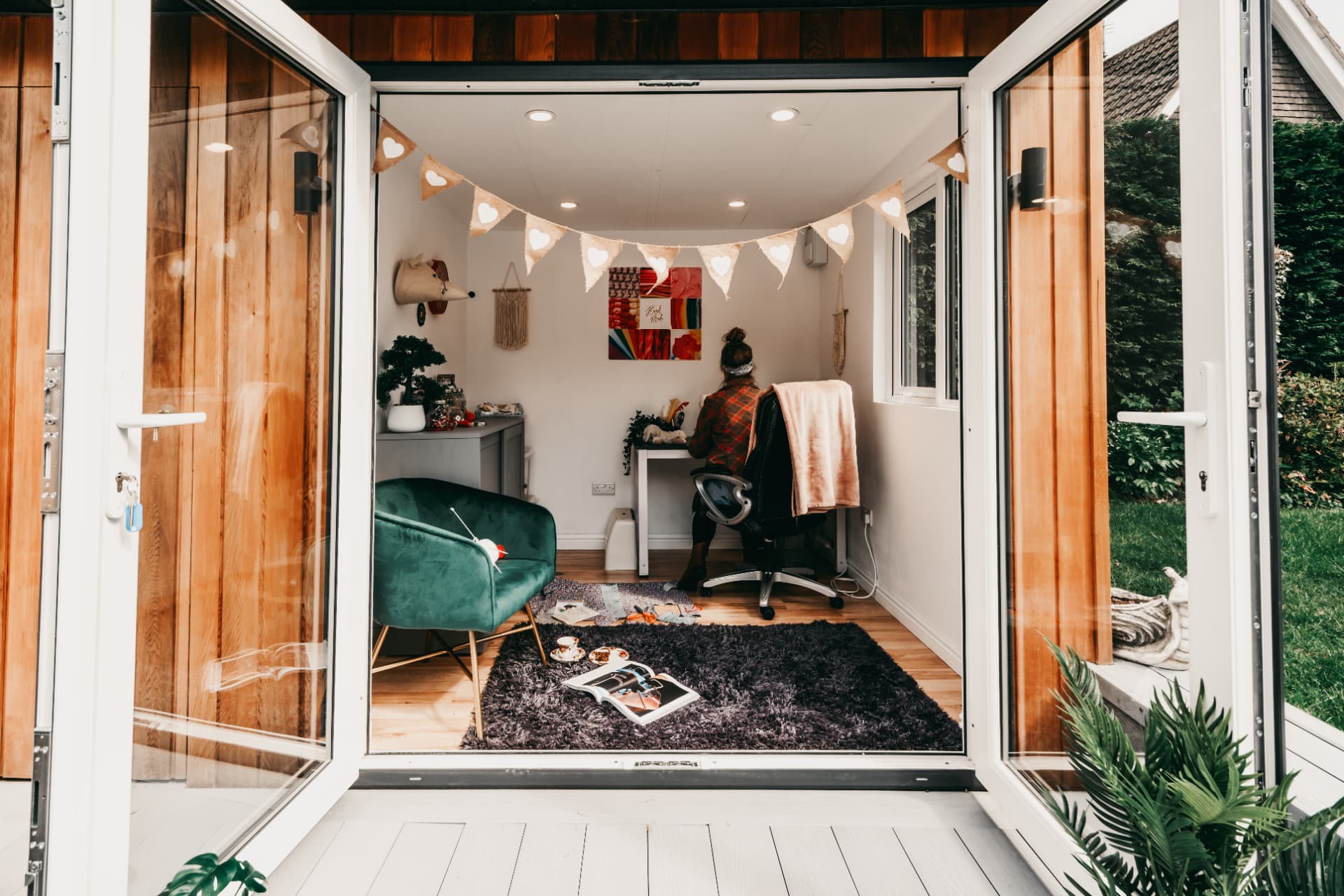 Cedar garden room used as a craft studio, seen through open French doors with bunting inside