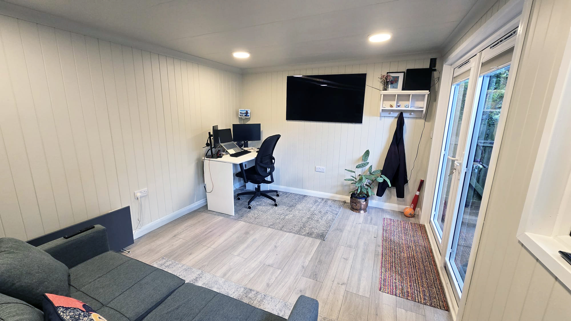 Garden room home office with desk, wall-mounted TV and sofa beside French doors