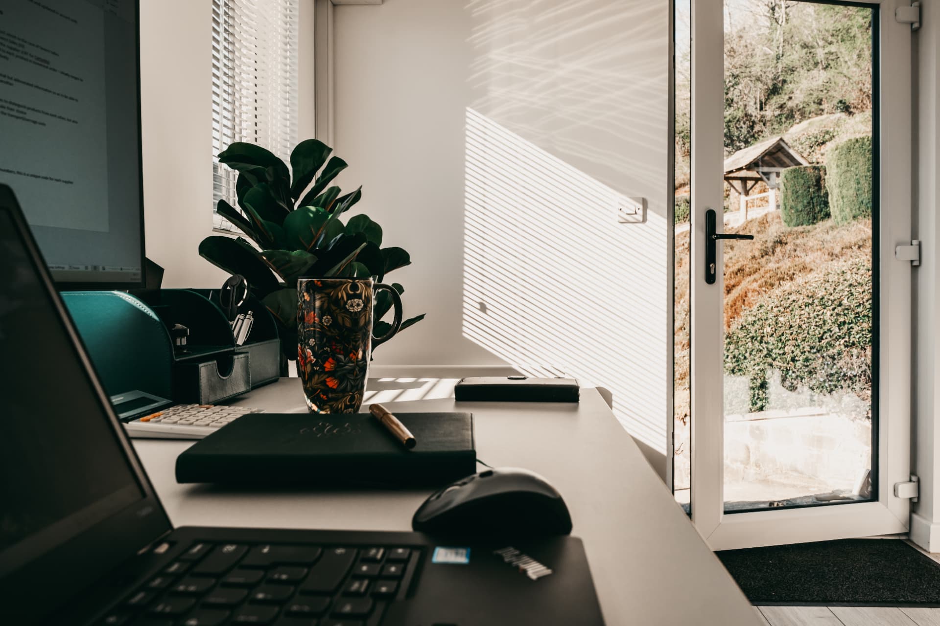 Garden office desk detail with laptop, plant and open door onto the garden