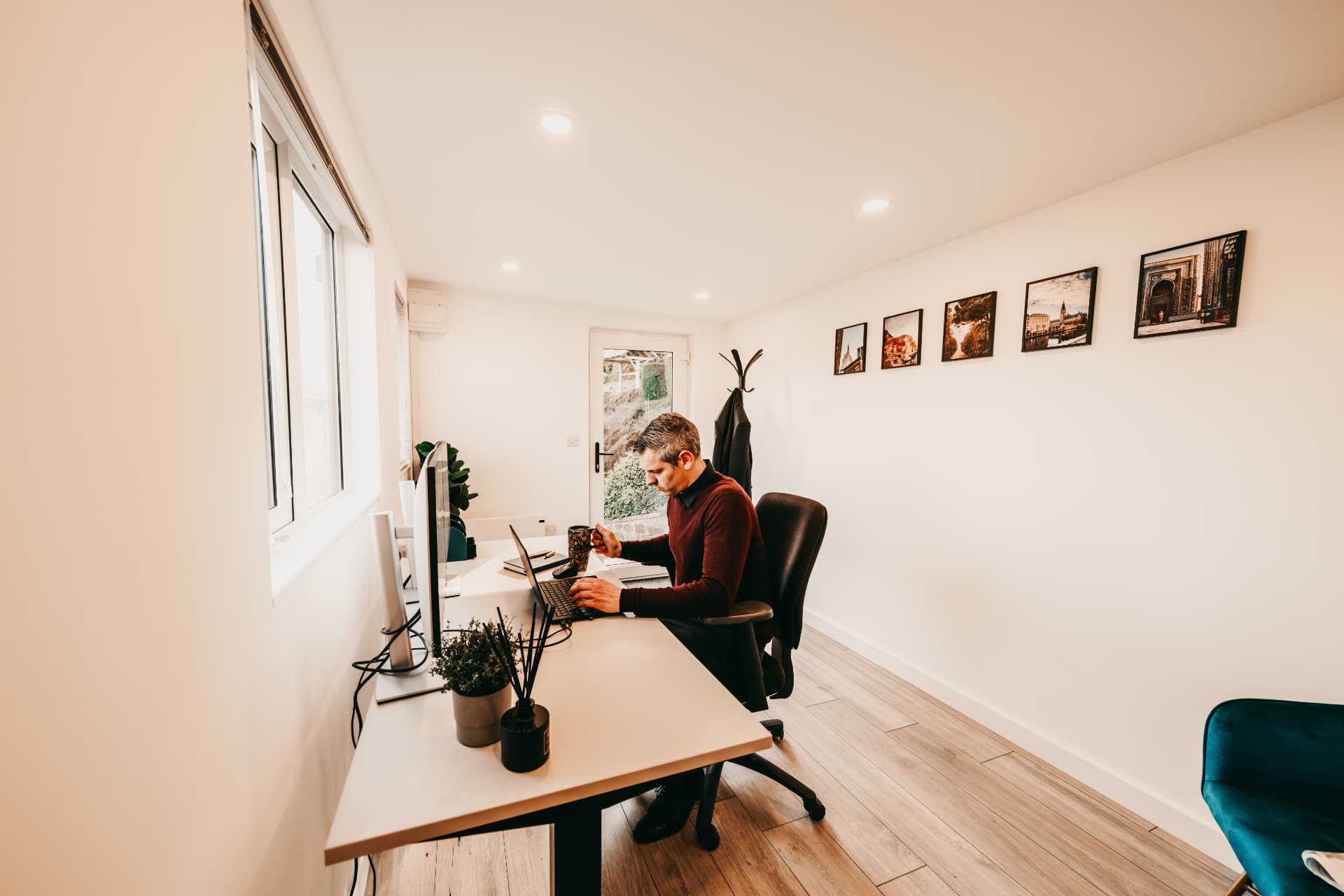 Long garden office with twin desks, framed photography and a velvet armchair
